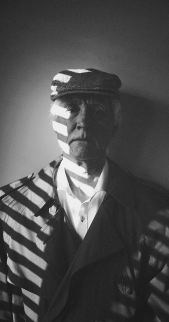 Man wearing a hat and trench coat with striped shadows.